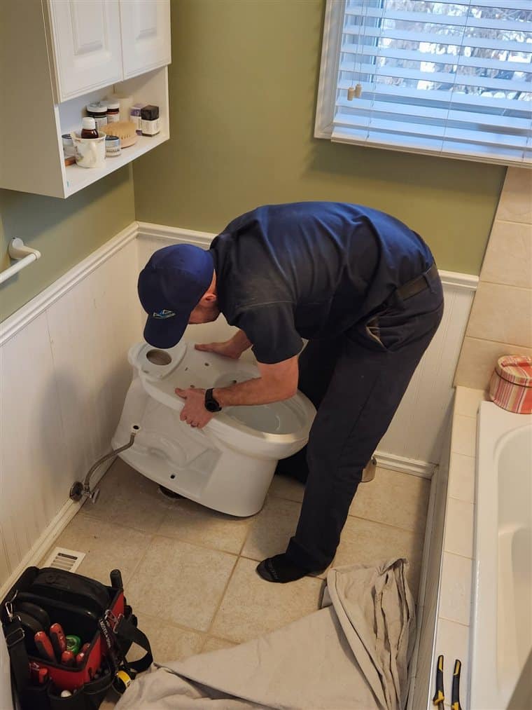 Ben from Accent Plumbing and Heating lifting a toilet off the flange in a Calgary bathroom