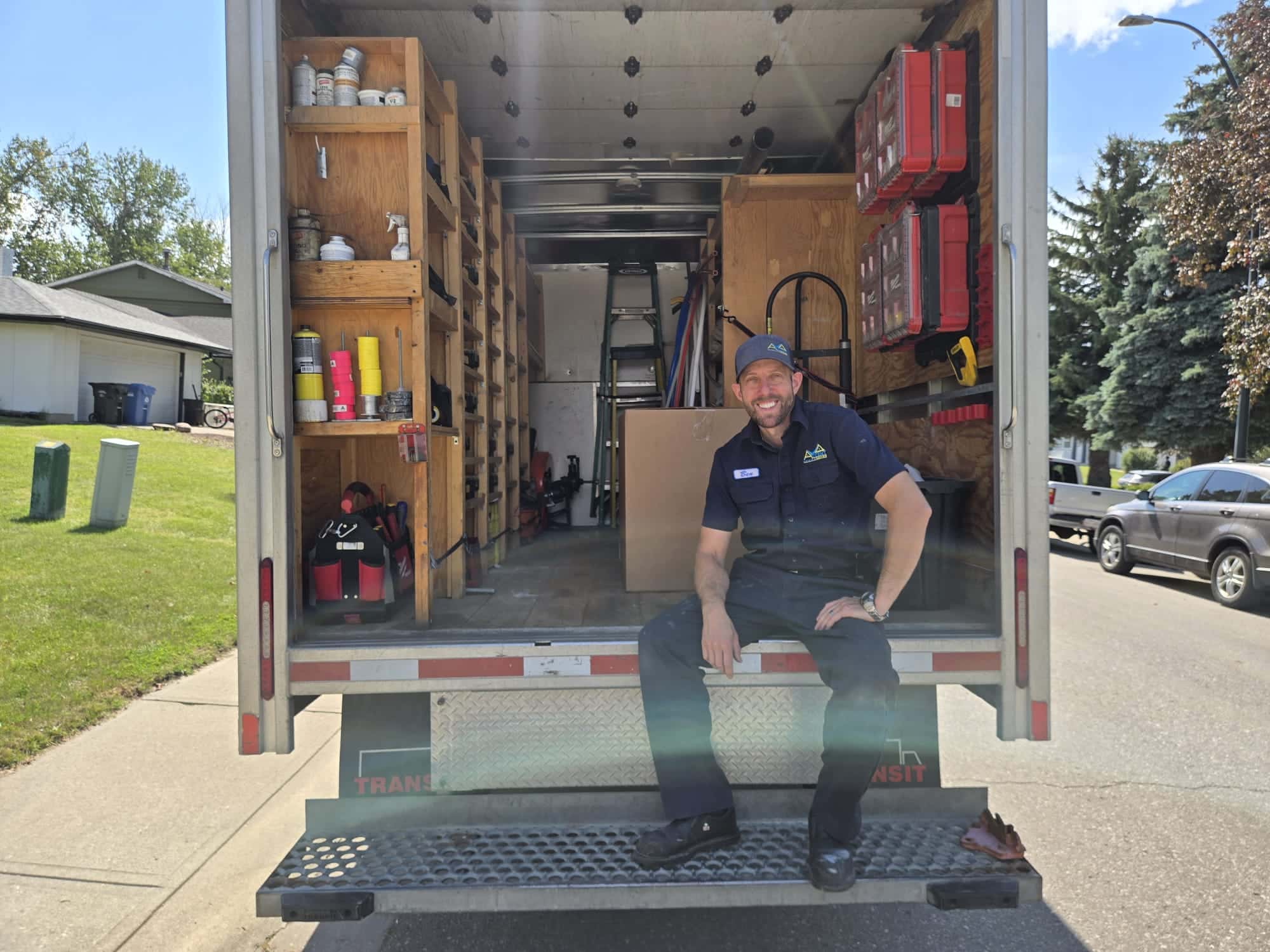 Ben Newman sitting on the tailgate of the Accent Plumbing and Heating van, doors open showing the stocked shelves