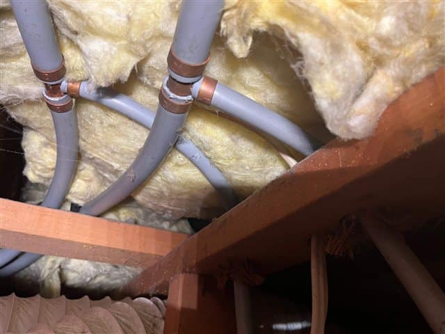 Grey poly-B water pipe with copper crimp rings on the fittings, in the ceiling of a Calgary mechanical room