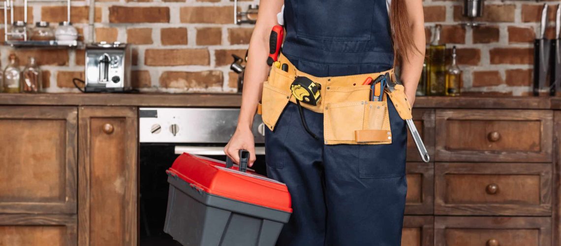 cropped shot of repairwoman with toolbox and toolbelt standing at kitchen